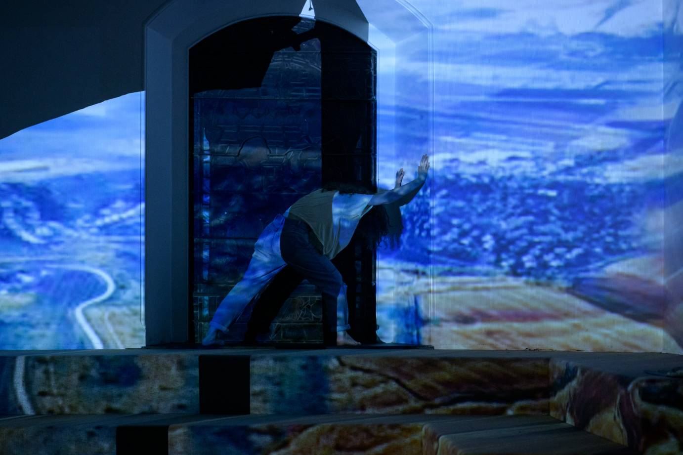 A woman lunges against a nave, drenched in a projection of a landscape